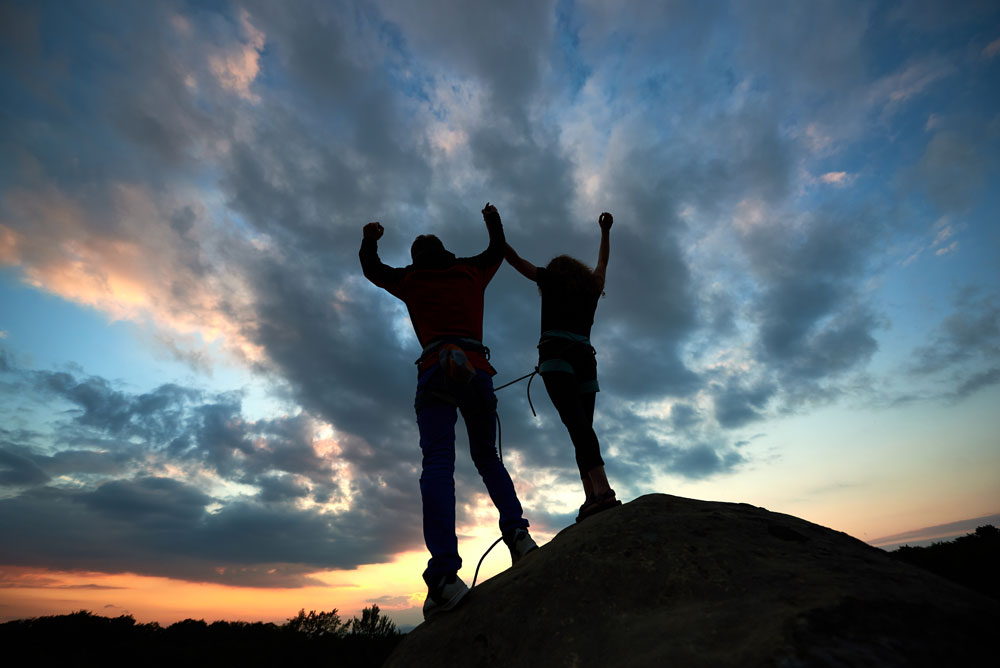 2 people on a hill celebrating during sunset.